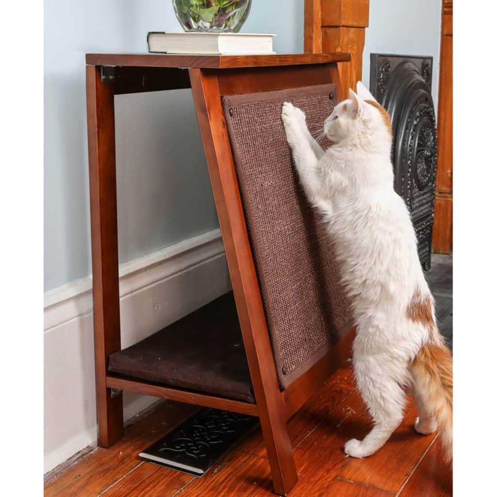 A white and orange cat scratches a brown, angled A-Frame Cat Bed on hardwood floors in a modern room.