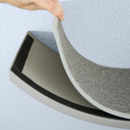 A hand lifts a gray carpeted pad from a curved Lotus Leaf Cat Shelf mounted on a light-colored wall.
