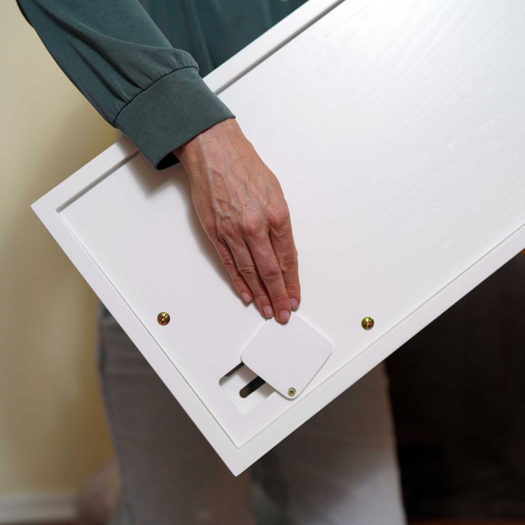 A person attaches a small white RSCLBC-Litter-Catch bracket to the back of a white wooden panel with their right hand.
