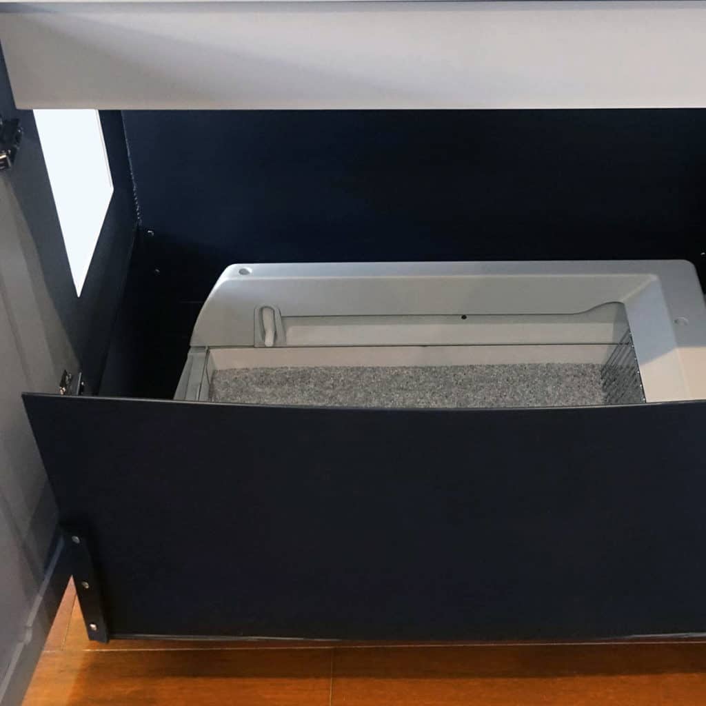 A black extra-large litter liner fits inside a dark blue cabinet's open built-in litter box on a wooden floor.