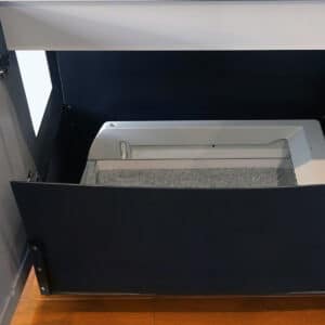 A black extra-large litter liner fits inside a dark blue cabinet's open built-in litter box on a wooden floor.
