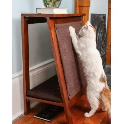 White cat with orange spots scratches a mahogany A-frame cat bed that doubles as a side table on hardwood floors.