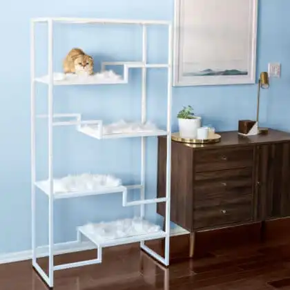 Modern white metal cat condo with faux fur pads beside a wooden dresser in a light blue room; cat on top shelf.