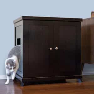 Gray and white cat exits a dark wood litter box with side opening on hardwood floor, next to a light blue wall.