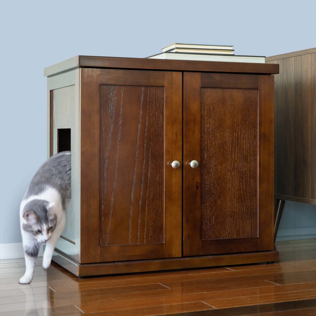 Gray and white cat steps out of a wooden cabinet-style litter box on a hardwood floor against a wall.