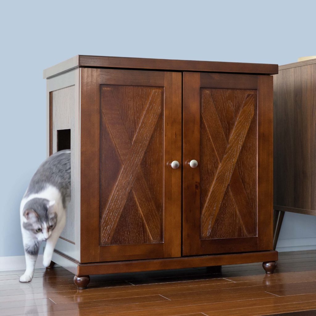 Gray and white cat exits a side opening in a double-door litter box cabinet on hardwood floor near a light blue wall.