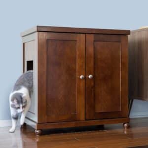 Gray and white cat stepping out of a round litter box cabinet with a side opening on hardwood against a light blue wall.