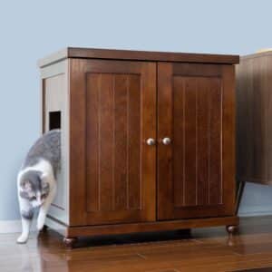 Gray and white cat steps out of a side-opening litter box cabinet on hardwood floor by a light blue wall.