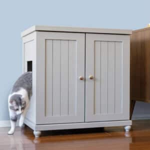 Gray and white cat steps out of a light gray cabinet-style litter box on a wooden floor.