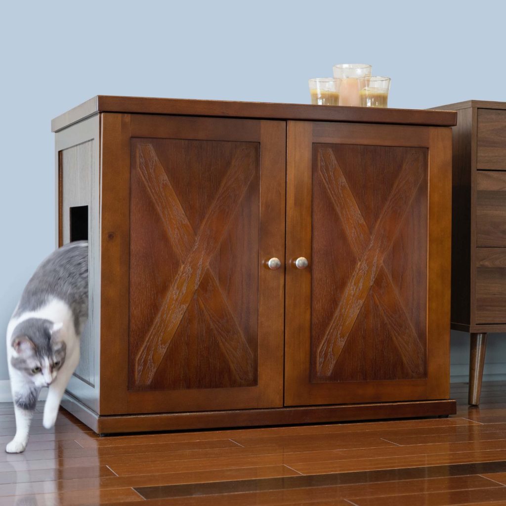 Gray and white cat leaving a gray and white cabinet with double X-panel doors, candles on top, on wooden floor.