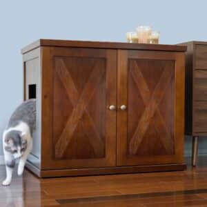 Gray and white cat leaving a gray and white cabinet with double X-panel doors, candles on top, on wooden floor.