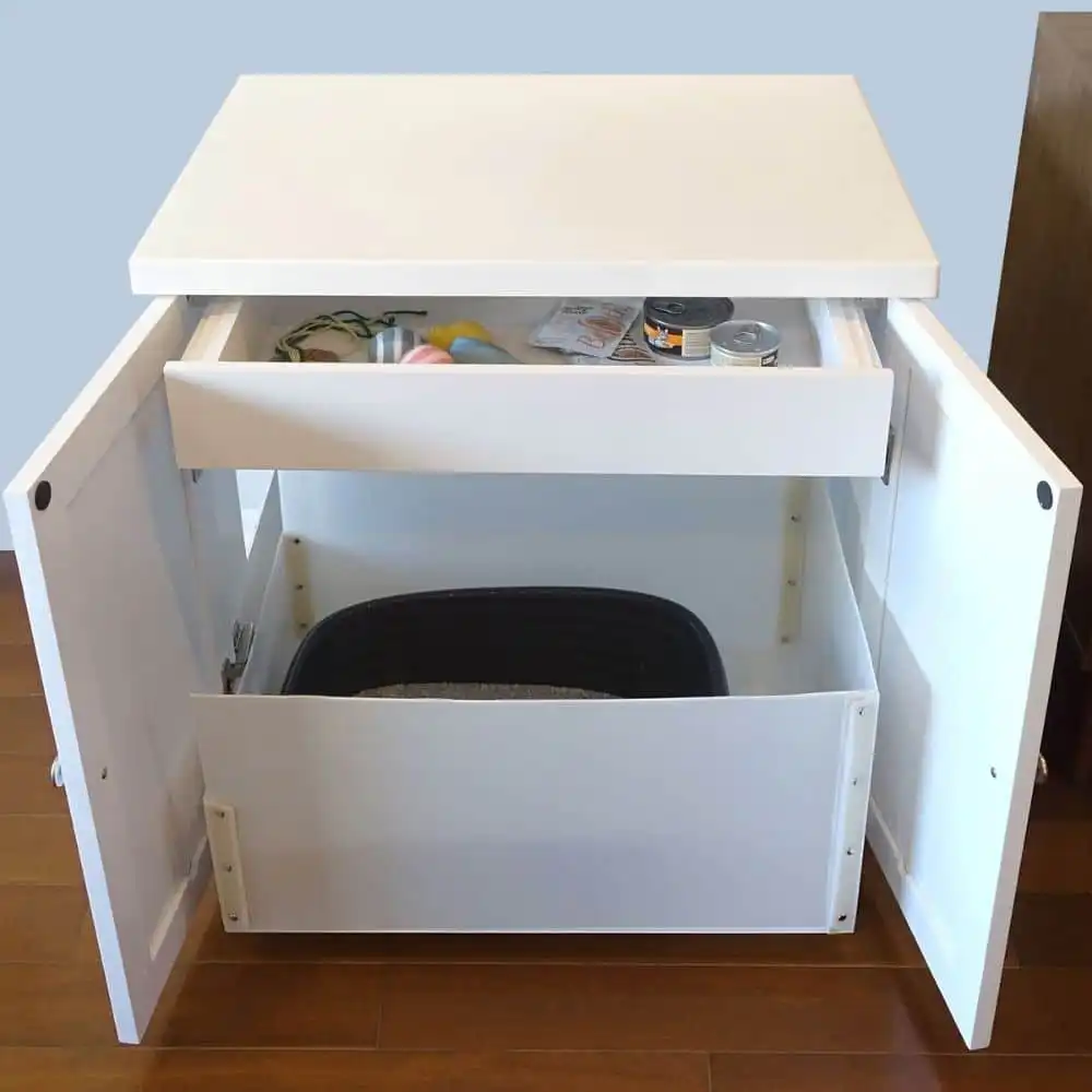 White litter box enclosure with open doors and drawer, showing a black litter box and organized pet supplies above.