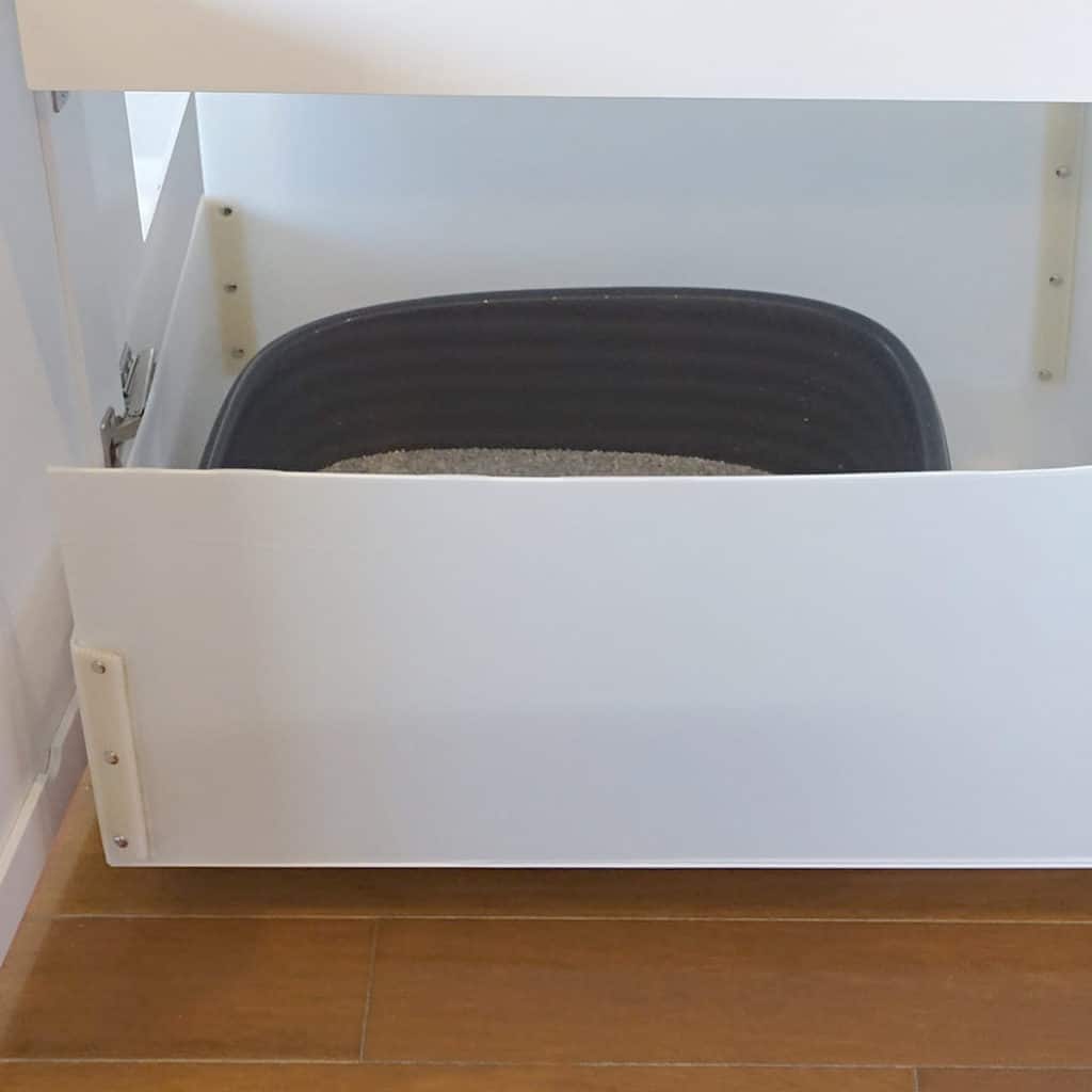 Large black litter box with sand in a pull-out white cabinet drawer, featuring an easy-to-replace liner.