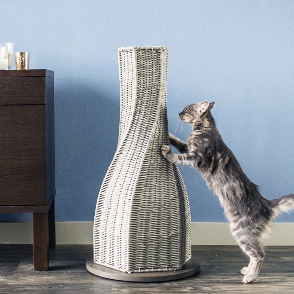 A cat stretches on a tall, woven scratching post next to a dark wooden cabinet against a blue wall.