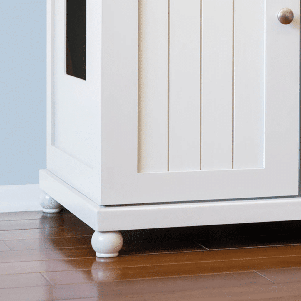 Deluxe white cabinet with panel door, round knob and feet, side rectangular opening, on a hardwood floor.