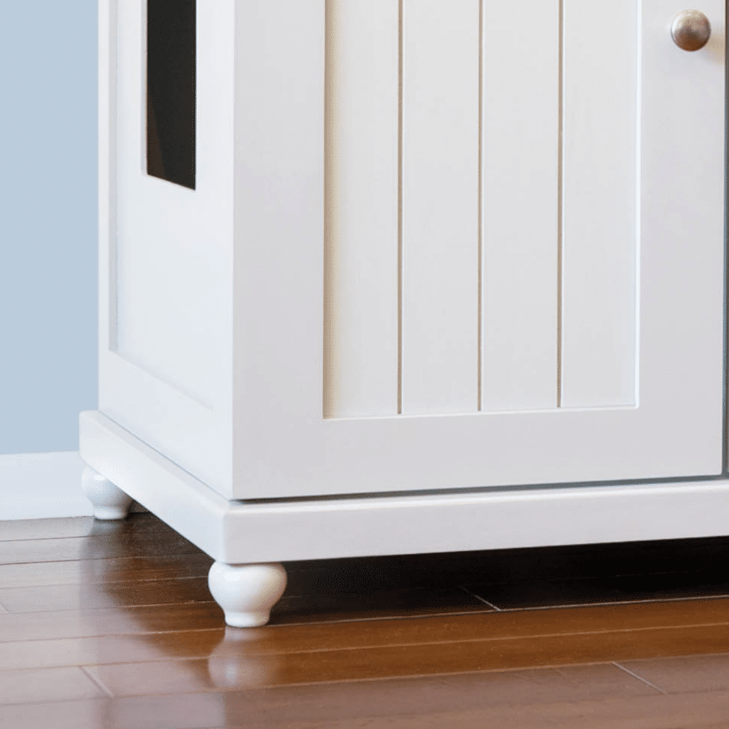 White wooden cabinet with paneled door and round knob, on four tulip-style feet, on wood floor against light blue wall.