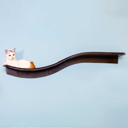 A white and orange cat lounges on a mahogany wave-shaped wall shelf resembling a branch, against a light blue background.