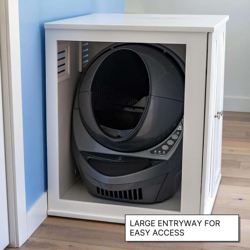 A black self-cleaning cat litter box sits inside a white cabinet with a sign reading "Large entryway for easy access.