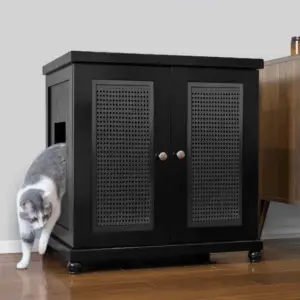 Gray and white cat stepping out of a black cabinet with mesh doors on a wooden floor next to wooden furniture.