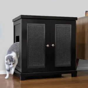 A gray and white cat exits a side opening of a black cabinet with double doors and paneling on a wooden floor.