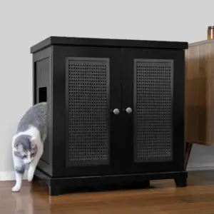 A gray and white cat exits a black wooden cabinet with a side entry hole, on a wood floor beside another furniture piece.
