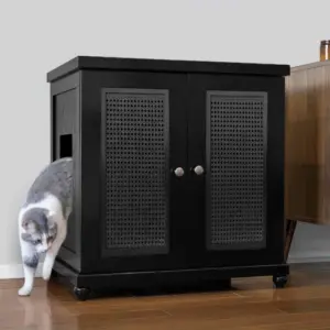 Gray and white cat walking out of a black cabinet with perforated doors on a wooden floor beside another cabinet.