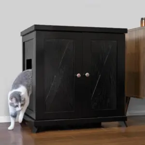 Gray and white cat leaves a black wooden cabinet with a side door on a wooden floor next to another piece of furniture.