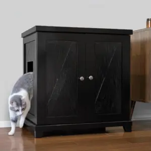 Gray and white cat stepping out of a black wooden cabinet with side entry on hardwood floor next to another cabinet.