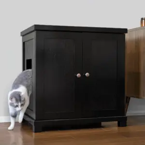 A gray and white cat exits a side opening of a black two-door wooden cabinet in a room with hardwood floors.