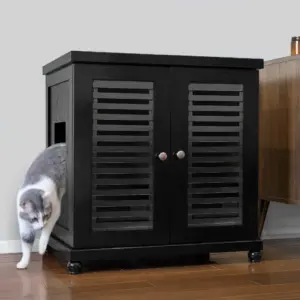 Gray and white cat exits a black wooden cabinet with slatted doors on a hardwood floor beside brown furniture.