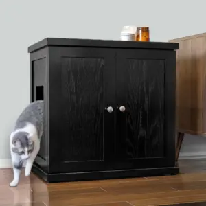 A gray and white cat steps out from a black wooden cabinet with a side opening; jars sit on top, near a wooden table.