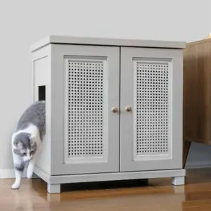 A gray and white cat steps out of a light gray, two-door cabinet with decorative panels on a wooden floor.