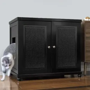 A gray and white cat leaves a black cabinet with a side opening on a wooden floor next to another piece of furniture.