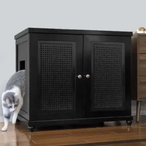 Gray and white cat steps out of a rectangular hole on the side of a black cabinet with two doors, on a wooden floor.