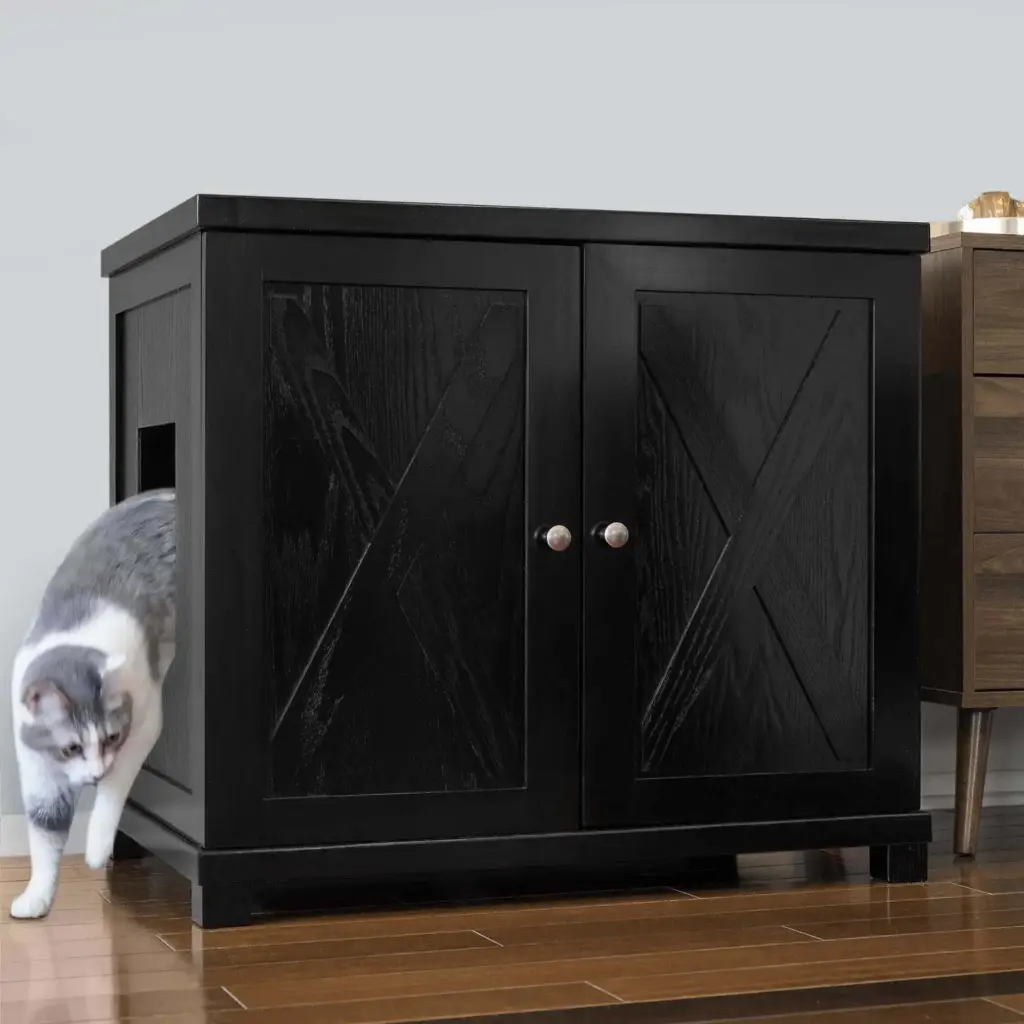Gray and white cat leaving the side opening of a black cabinet with double doors on a wooden floor beside furniture.