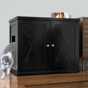 Gray and white cat leaving a black double-door cabinet with side opening on wooden floor beside another piece of furniture.