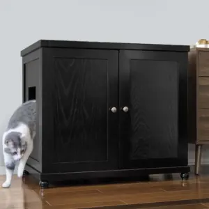 Gray and white cat steps out of a black cabinet with a side opening onto hardwood floor next to another furniture piece.