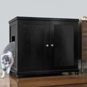 Gray and white cat exits side opening of black wooden cabinet with double doors on a wooden floor beside furniture.