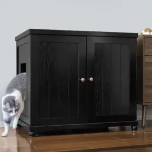 Gray and white cat exits side opening of black cabinet with double doors on wood floor beside small brown dresser.