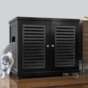 A gray and white cat steps out of a black cabinet with slatted doors on a hardwood floor beside another piece of furniture.
