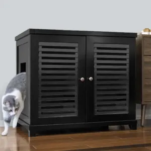 Gray and white cat walking out of a black cabinet with slatted doors on a wooden floor next to other furniture.