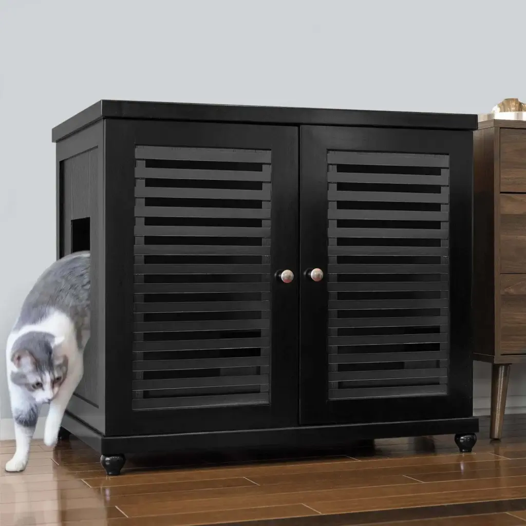 Gray and white cat exits side opening of black cabinet with two vented doors, set on a hardwood floor.