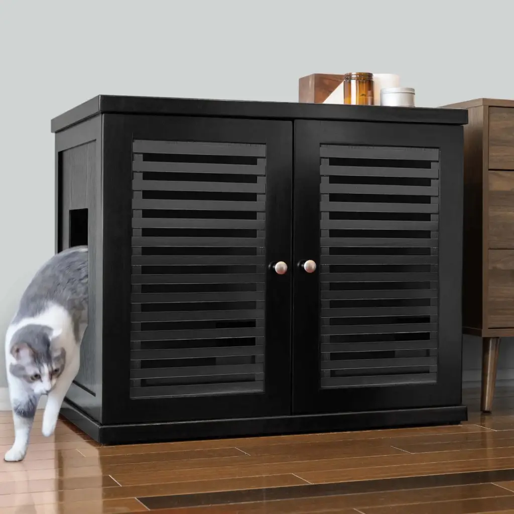 Gray and white cat steps out of a black slatted-door cabinet on wooden floor; candles are placed on top of the cabinet.